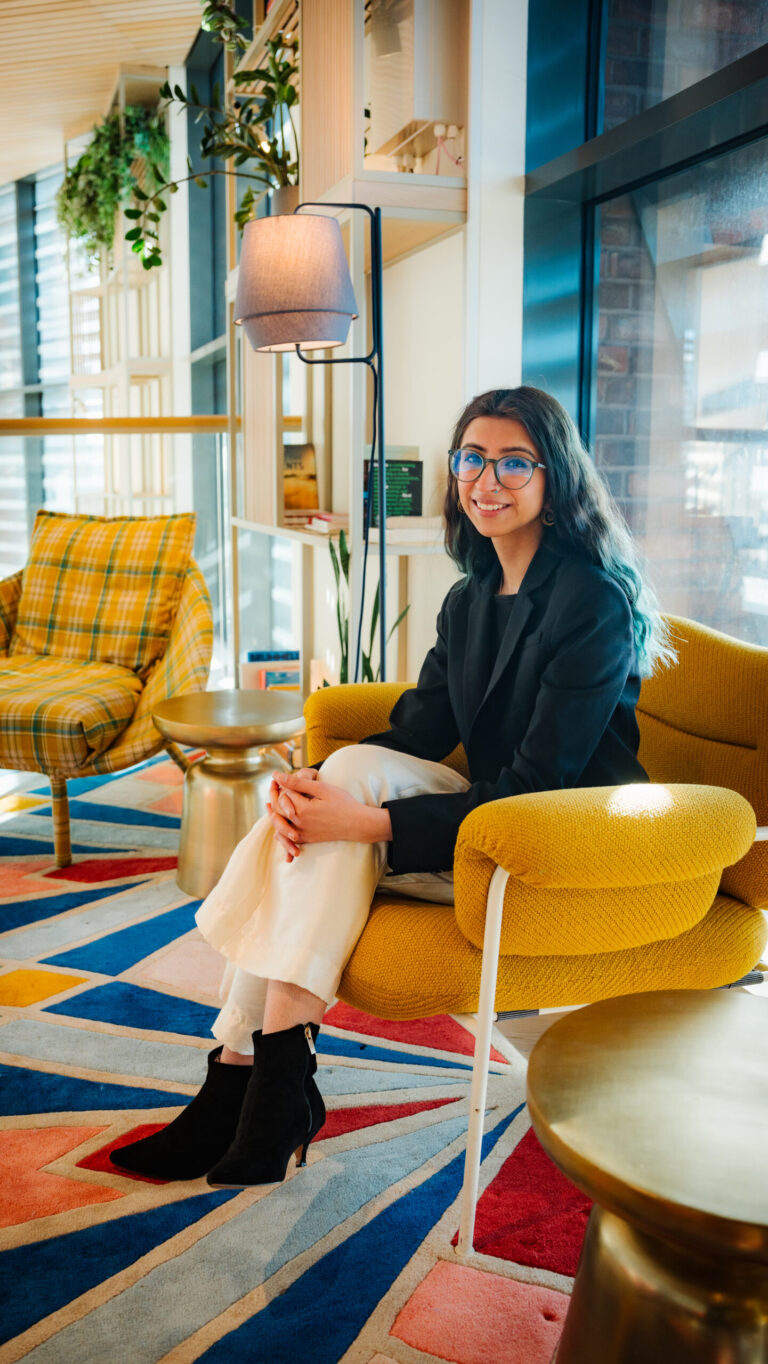 Pearl seated on a yellow chair, on a colourful patterned rug